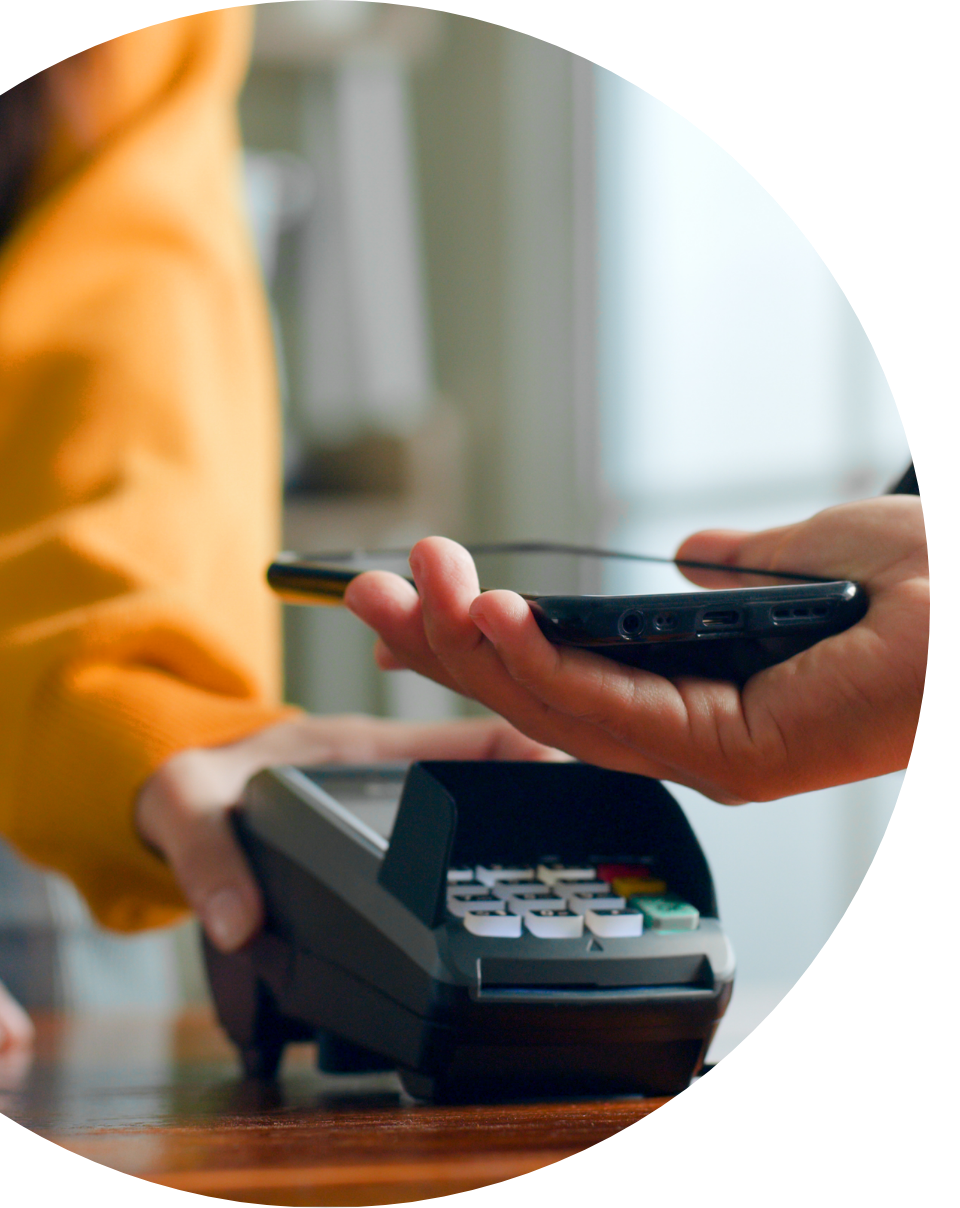 Hand holding smartphone over card reader for tap to pay contactless transaction at checkout counter
